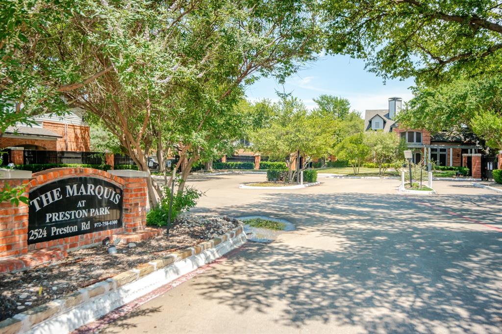 2524 Preston Road, Unit 808 Plano, TX 75093 - Photo 29 of 31 Gated community entrance featuring a brick monument sign, mature trees providing canopy, paved drive, and residential structures in the background