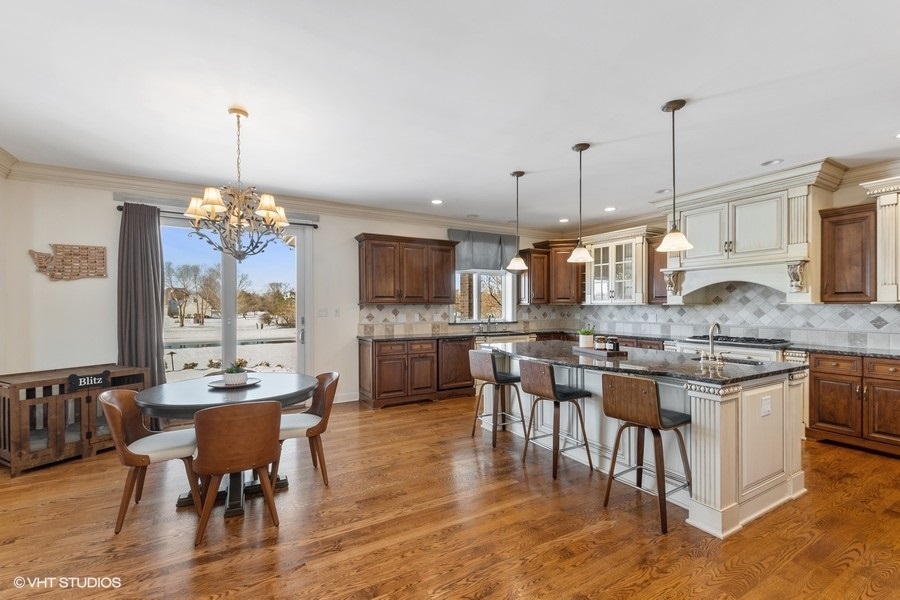 24042 Old Farm Road Manhattan, IL 60442 - Photo 6 of 32 a open kitchen with stainless steel appliances granite countertop a stove top oven a sink a dining table and chairs with wooden floor