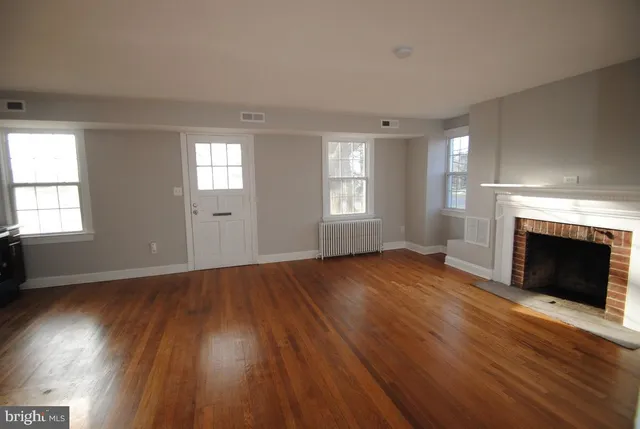 an empty room with wooden floor fireplace and windows