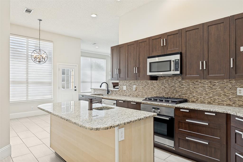 2100 Los Rios Boulevard Plano, TX 75074 - Photo 10 of 25 Kitchen featuring an island with a sink, stainless steel appliances, dark wood-finish cabinetry, a tiled backsplash, and recessed lighting