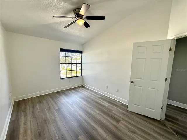 an empty room with wooden floor ceiling fan and windows
