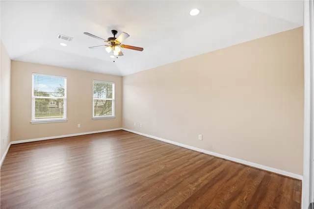 an empty room with wooden floor ceiling fan and windows