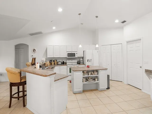a kitchen with stainless steel appliances a sink a stove a refrigerator cabinets and chairs