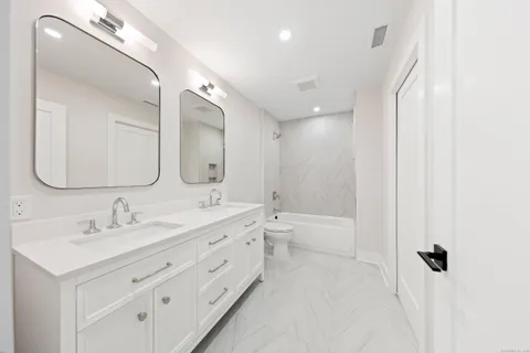a spacious bathroom with a double vanity sink toilet mirror and bathtub