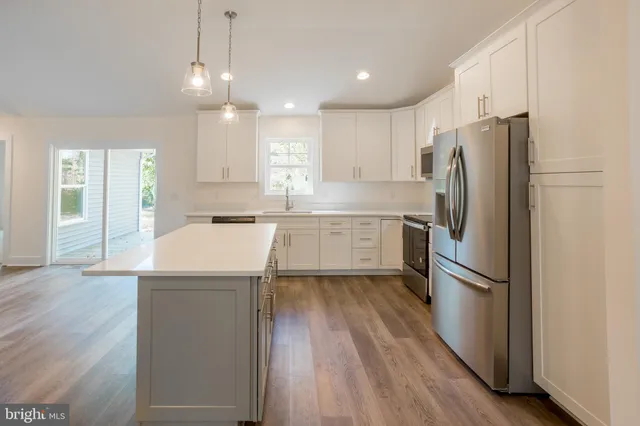 a kitchen with kitchen island a refrigerator a sink dishwasher a stove and white cabinets with wooden floor