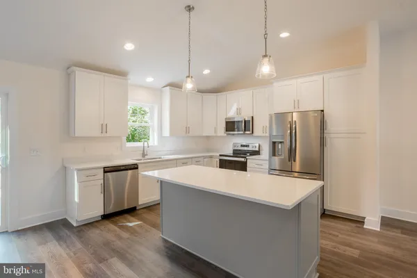 a kitchen with stainless steel appliances a refrigerator a sink dishwasher a stove top oven a kitchen island with wooden floor and cabinets