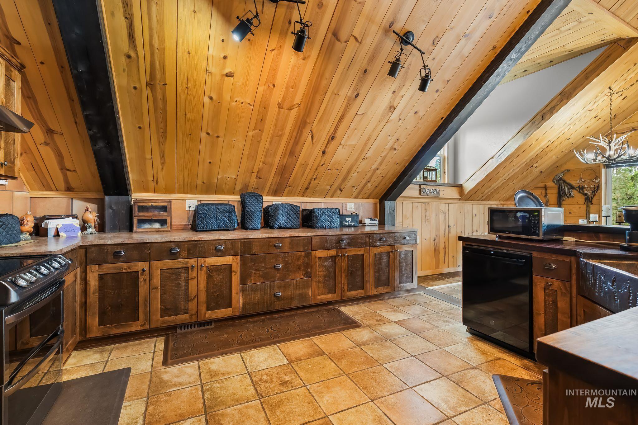 3989 East Mountain Road Anatone, WA 99401 - Photo 9 of 49 Vaulted wood-paneled ceiling with exposed beam, track lighting, wood-finish cabinetry, tile flooring, and integrated black appliances