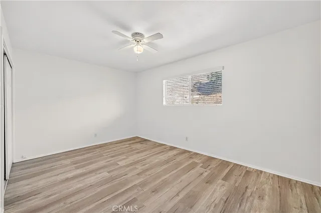 a view of an empty room with wooden floor and a fan