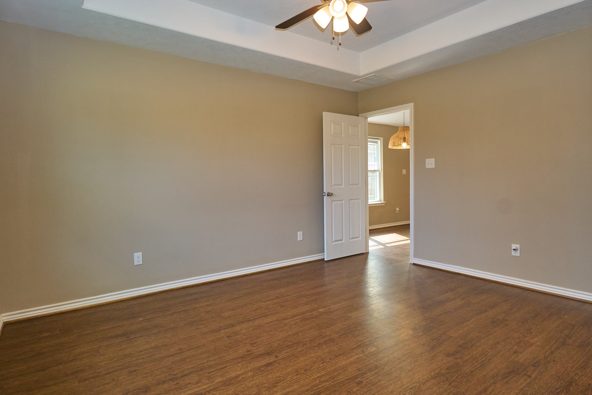 1807 Nuches Lane Bryan, TX 77803 - Photo 15 of 27 This room features warm wood flooring, neutral walls, a ceiling fan with lights, and a tray ceiling. An open door leads to a brightly lit adjacent area with a window.