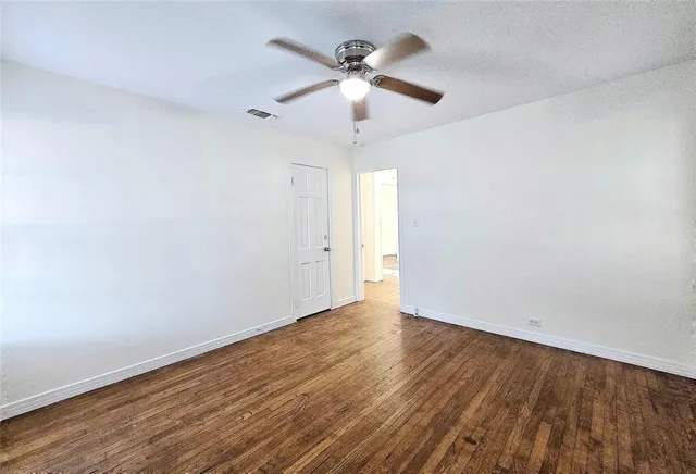 an empty room with wooden floor ceiling fan and windows