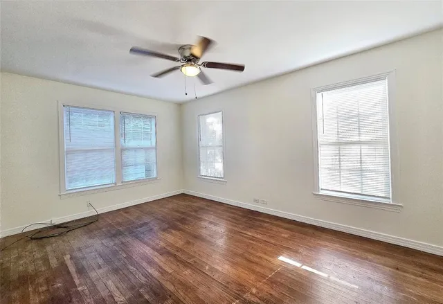 an empty room with wooden floor fan and windows