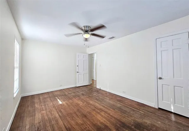 an empty room with wooden floor fan and windows