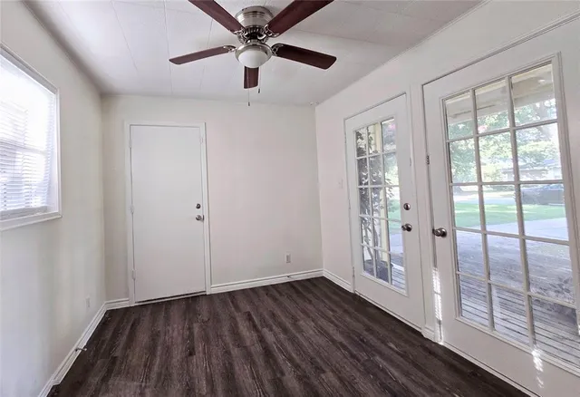an empty room with wooden floor fan and windows