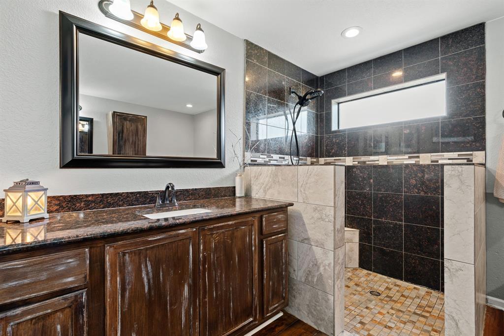 5058 West Highway 199 Springtown, TX 76082 - Photo 27 of 40 a bathroom with a granite countertop sink a mirror and a shower