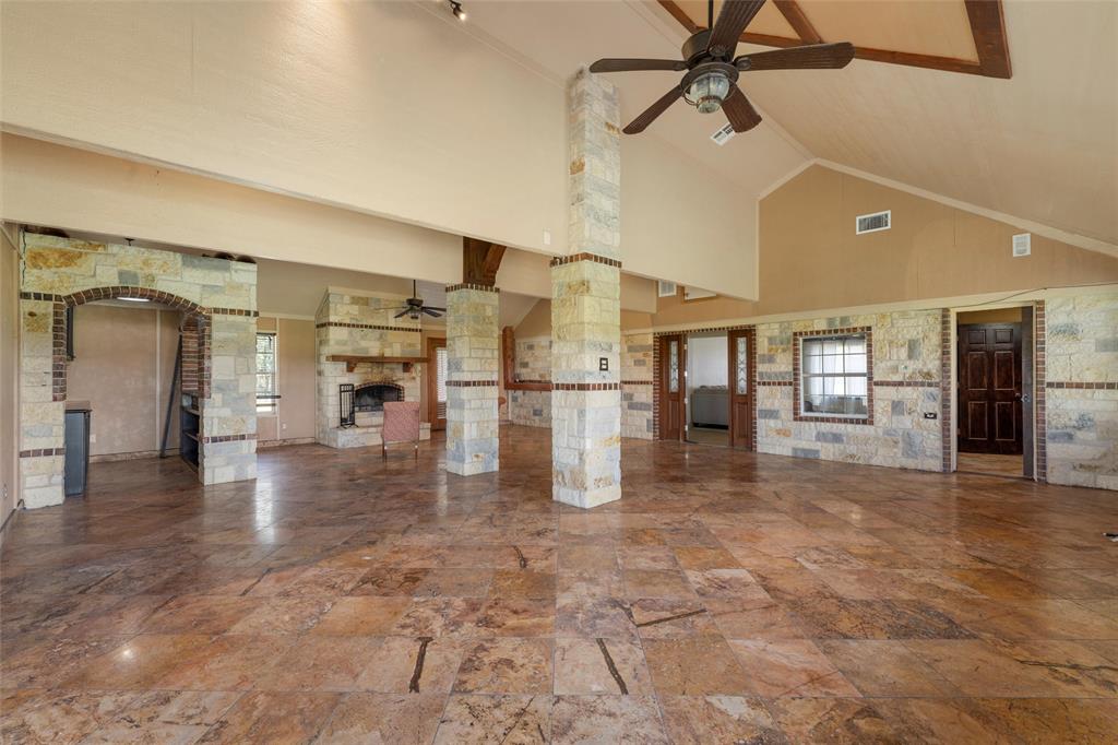 3433 West Tours Road West, TX 76691 - Photo 19 of 40 Unfurnished living room featuring high vaulted ceiling, a fireplace, a ceiling fan, stone tile floors, and decorative columns