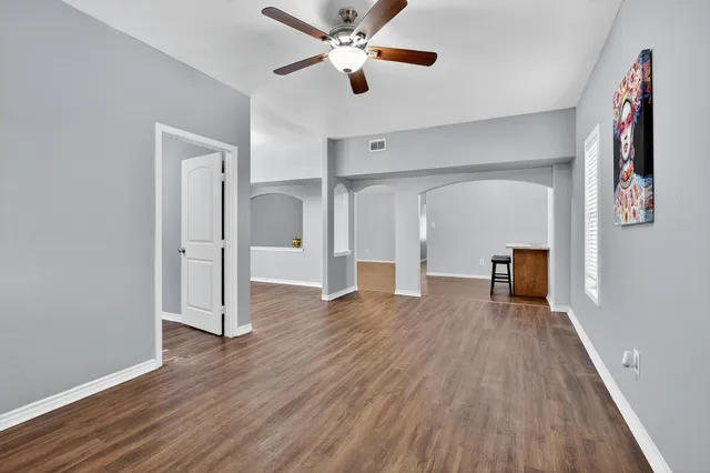an empty room with wooden floor chandelier fan and windows