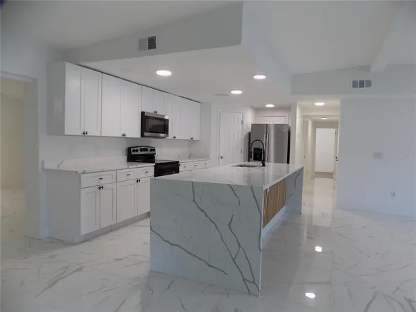 a living room with stainless steel appliances kitchen island granite countertop a refrigerator and a stove top oven