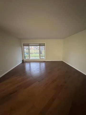 a view of an empty room with wooden floor and window