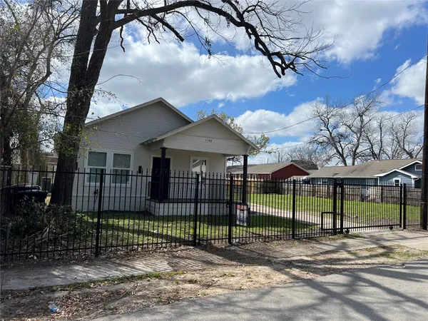 a view of a white house with a large tree and wooden fence