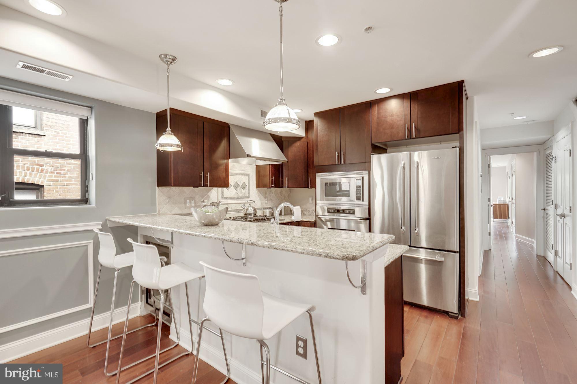 a kitchen with stainless steel appliances kitchen island granite countertop a refrigerator a sink dishwasher a stove and a refrigerator with wooden floor