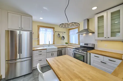 a kitchen with stainless steel appliances granite countertop a refrigerator a sink dishwasher a stove and white cabinets with wooden floor