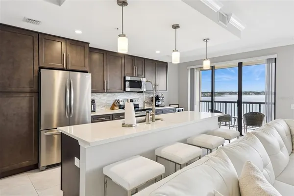 a kitchen with stainless steel appliances granite countertop a refrigerator a sink dishwasher a kitchen island with couches chairs and wooden floor