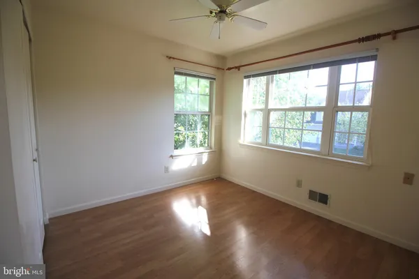 an empty room with wooden floor chandelier fan and windows