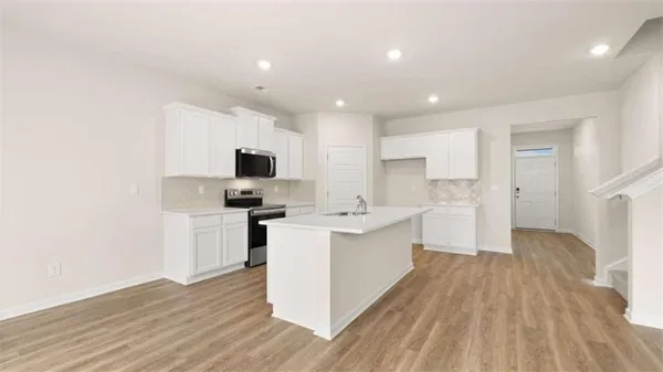 a kitchen with stainless steel appliances granite countertop a stove top oven a sink a refrigerator and white cabinets with wooden floor