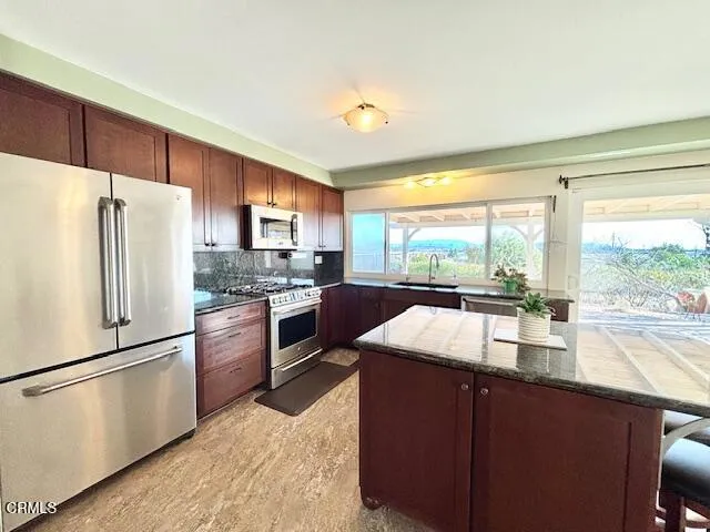 a kitchen with stainless steel appliances granite countertop a refrigerator a stove and a sink with large window