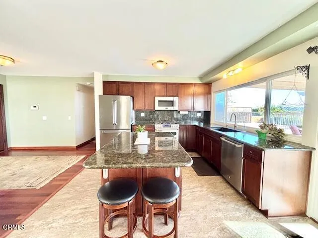 a kitchen with stainless steel appliances granite countertop a stove a refrigerator a sink and a dining table with wooden floor