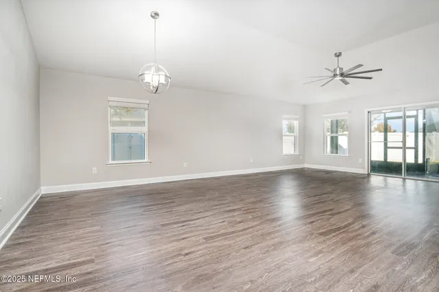 an empty room with wooden floor ceiling fan and windows