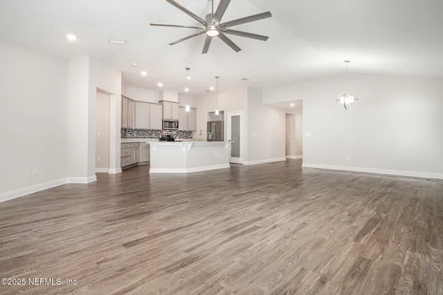 a view of an empty room and kitchen with wooden floor