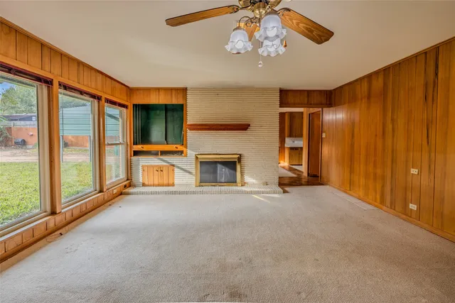 a view of a livingroom with a fireplace a ceiling fan and windows