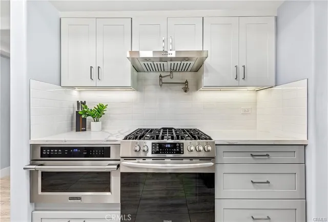a kitchen with granite countertop a stove a sink and a white wooden cabinets