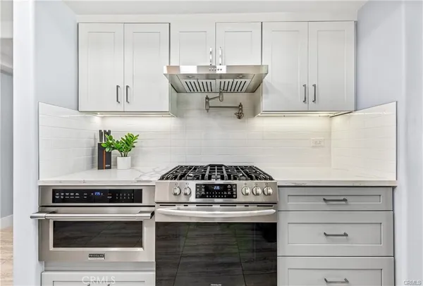 a kitchen with granite countertop a stove a sink and a white wooden cabinets