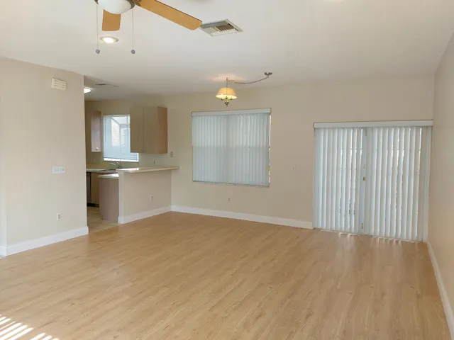 an empty room with wooden floor and kitchen view