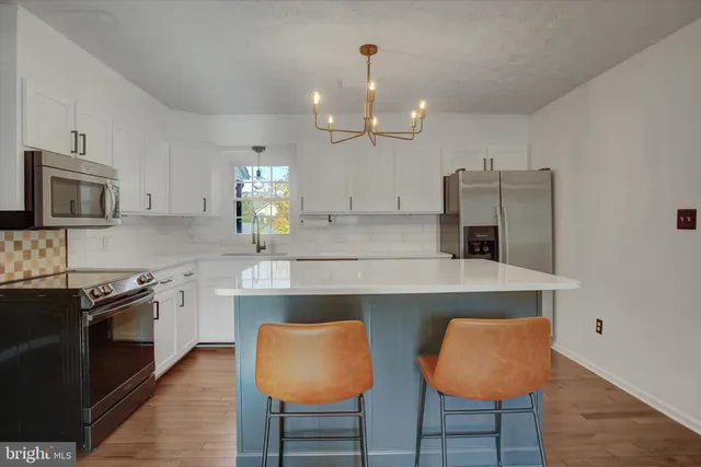 a kitchen with stainless steel appliances a sink a stove a refrigerator cabinets and chairs