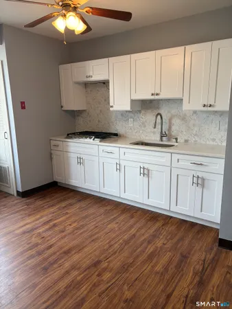 a kitchen with stainless steel appliances granite countertop a sink a stove and white cabinets with wooden floor