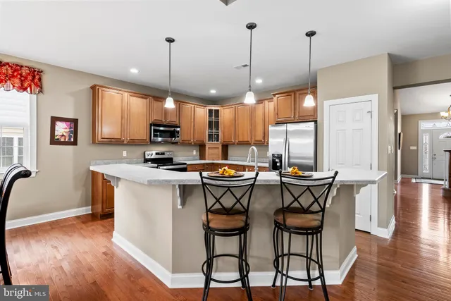 a kitchen with stainless steel appliances granite countertop a stove top oven a refrigerator a sink a dining table and chairs with wooden floor