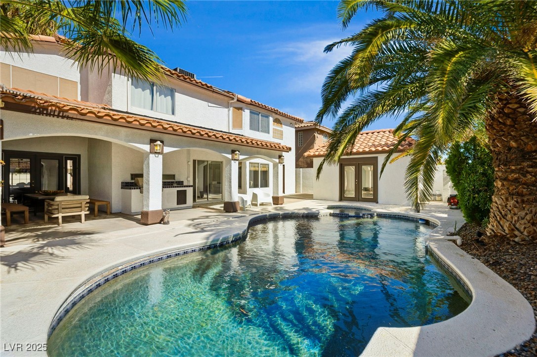 Rear view of house featuring french doors, an outdoor kitchen, an outdoor pool, and stucco siding