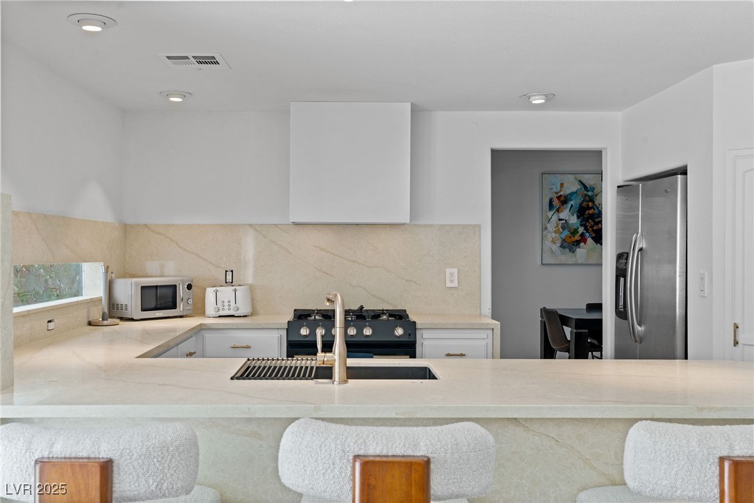 2829 Via Florentine Street Henderson, NV 89074 - Photo 6 of 48 Kitchen featuring stainless steel appliances, light stone countertops, decorative backsplash, and white cabinetry