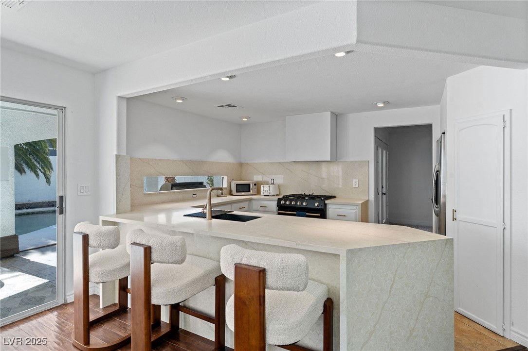 2829 Via Florentine Street Henderson, NV 89074 - Photo 7 of 48 Kitchen featuring light stone countertops, decorative backsplash, a peninsula, white cabinets, and black range with gas stovetop