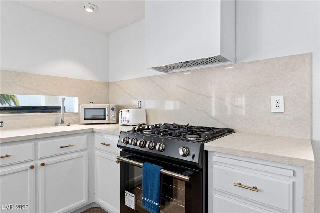 2829 Via Florentine Street Henderson, NV 89074 - Photo 8 of 48 Kitchen featuring gas stove, white cabinetry, custom exhaust hood, stainless steel microwave, and light stone counters