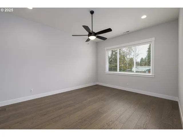 an empty room with wooden floor ceiling fan and windows