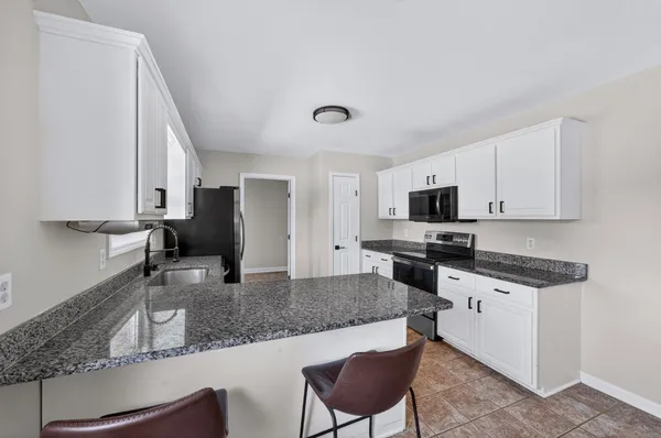 a kitchen with stainless steel appliances granite countertop a stove top oven a sink a dining table and chairs with white cabinets