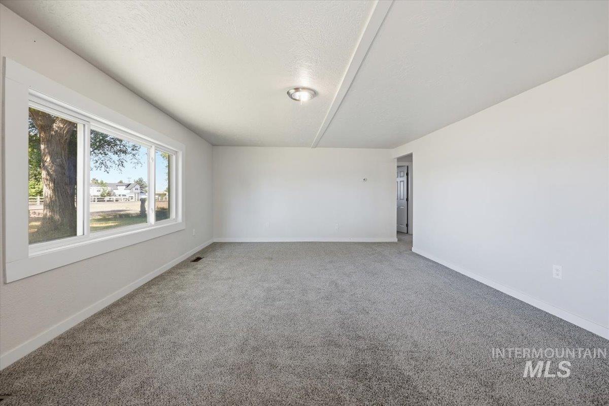 956 Southeast Hamilton Road Mountain Home, ID 83647 - Photo 11 of 34 Spacious room featuring neutral carpeting, white walls, a large multi-pane window with white trim, and a flush-mount ceiling light fixture