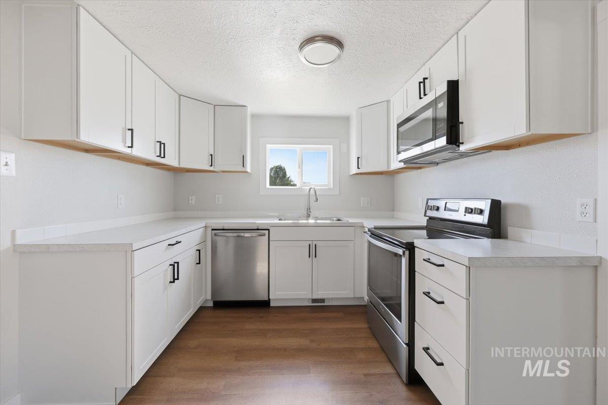 956 Southeast Hamilton Road Mountain Home, ID 83647 - Photo 15 of 34 U-shaped kitchen with white shaker-style cabinetry, light countertops, stainless steel appliances, and wood-finish flooring