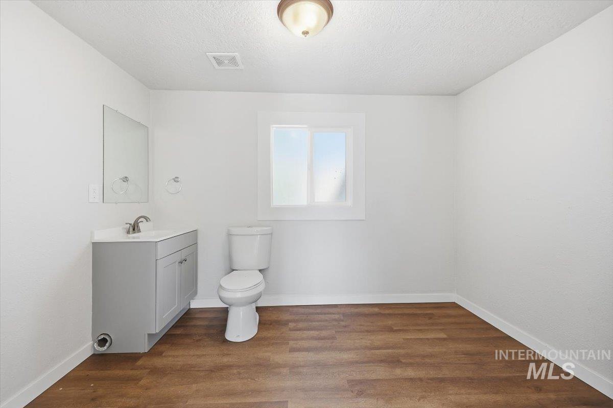 956 Southeast Hamilton Road Mountain Home, ID 83647 - Photo 19 of 34 Bathroom featuring wood-finish flooring, a contemporary gray vanity with an integrated sink, a white toilet, and a window providing natural illumination