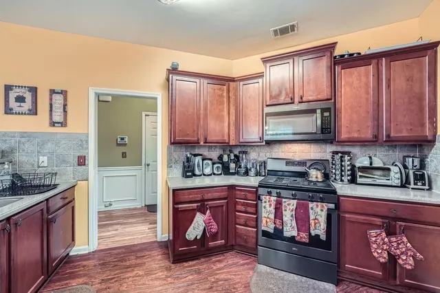 a kitchen with stainless steel appliances granite countertop a stove top oven a sink dishwasher and cabinets with wooden floor