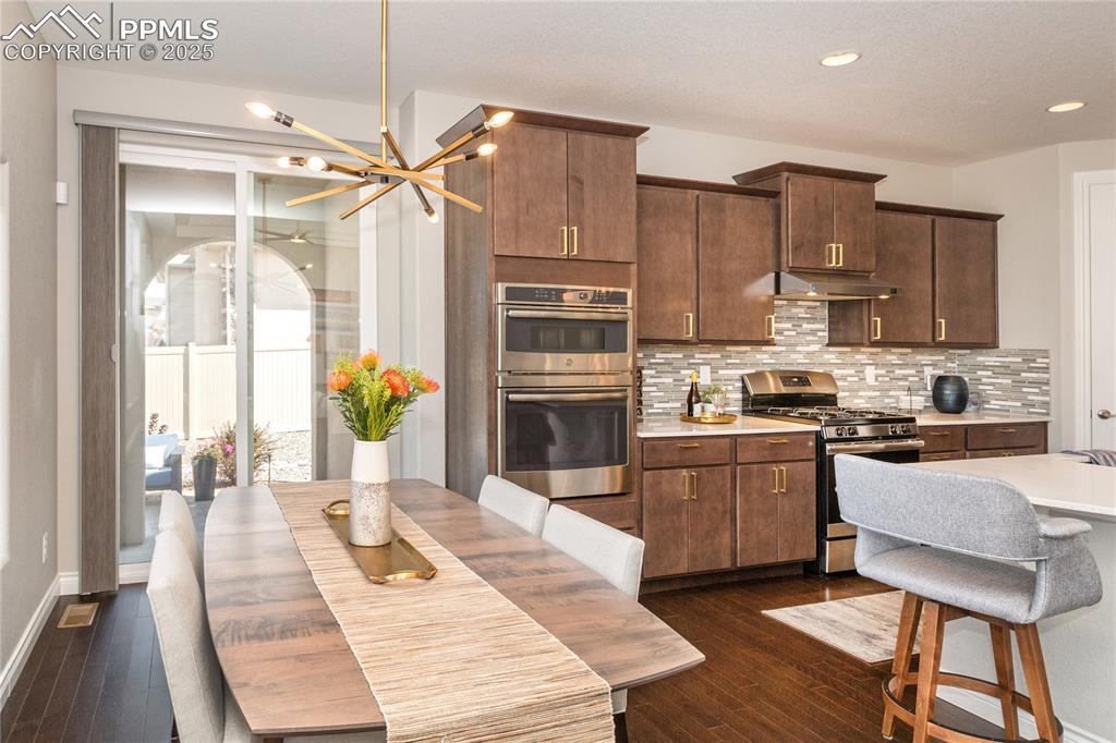 12516 Stone Valley Drive Peyton, CO 80831 - Photo 14 of 44 a kitchen with stainless steel appliances kitchen island granite countertop a refrigerator a stove top oven and a dining table with wooden floor